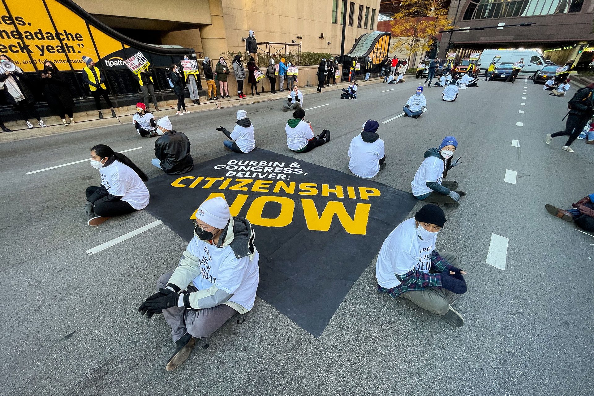 Manifestantes frente a la oficina de campo del Servicio de Inmigración y Control de Aduanas (ICE) en el centro de Chicago, con megáfonos y pancartas pidiendo una vía para la ciudadanía.