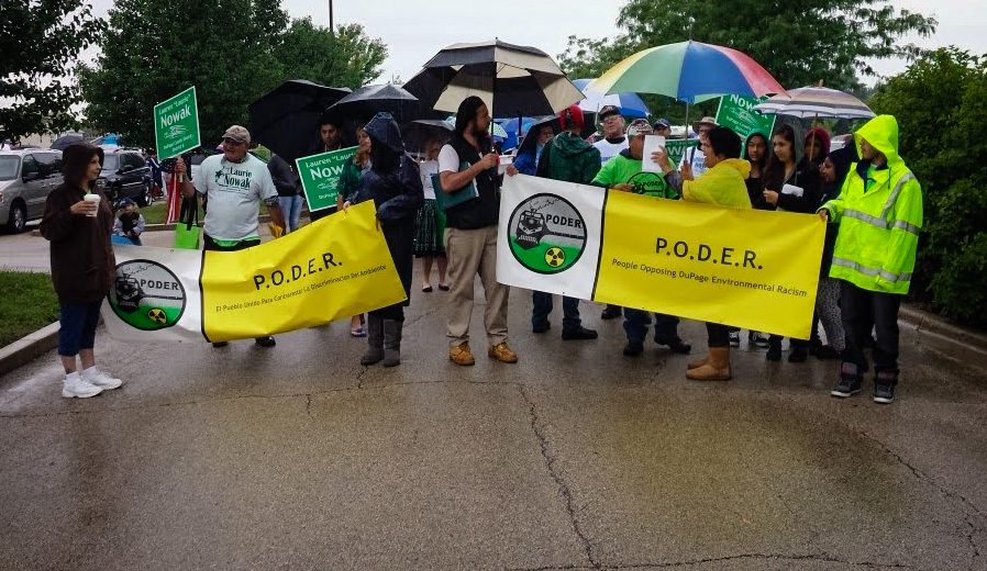 Miembros de Immigrant Solidarity DuPage marchan en la calle con pancartas que dicen P.O.D.E.R en un día lluvioso