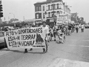 Immigrant rights march on 18th Street showing a large banner that says "alto a las deportaciones" "esta es mi tierra!" and "esta es mi lucha"