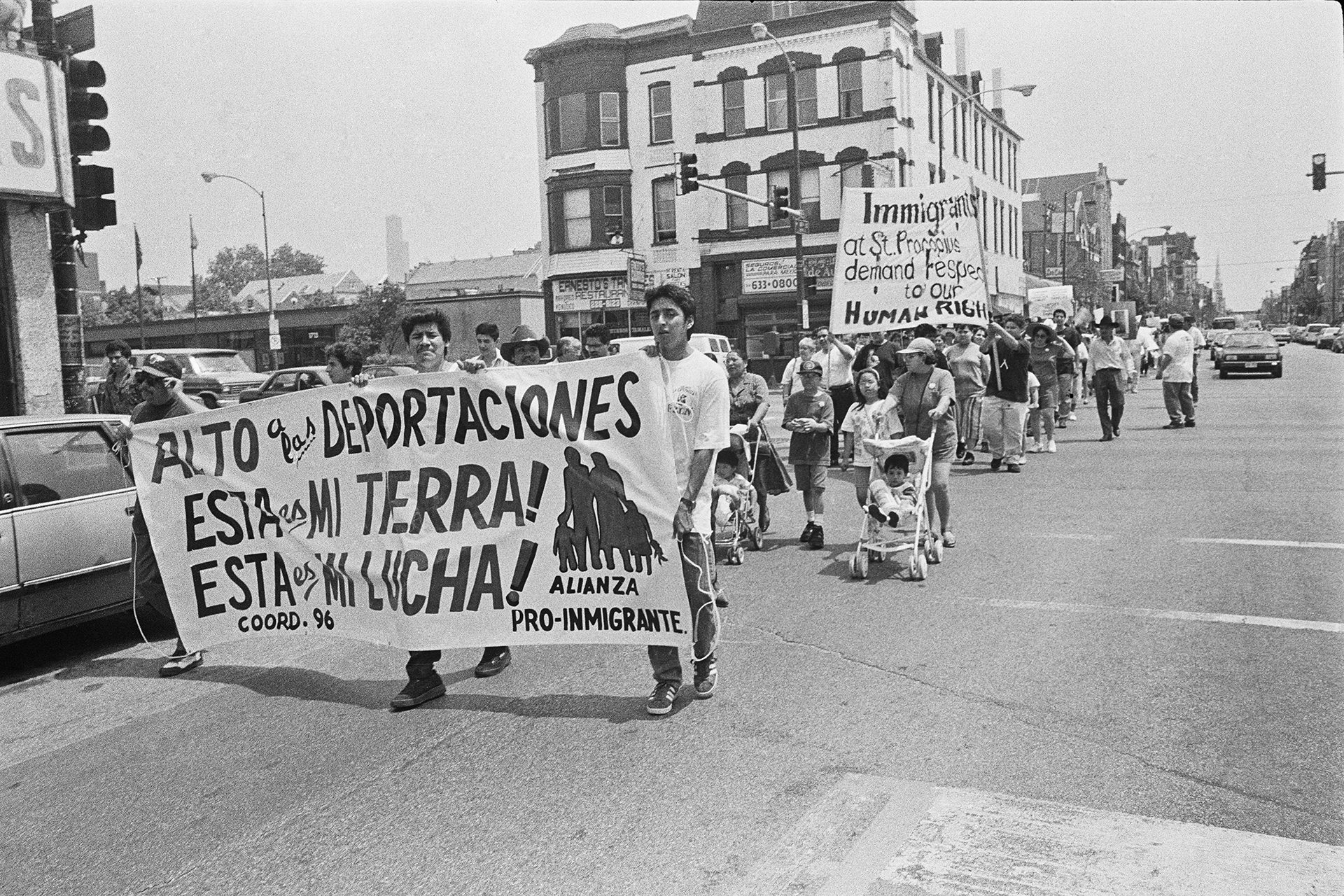 Immigrant rights march on 18th Street showing a large banner that says "alto a las deportaciones" "esta es mi tierra!" and "esta es mi lucha"