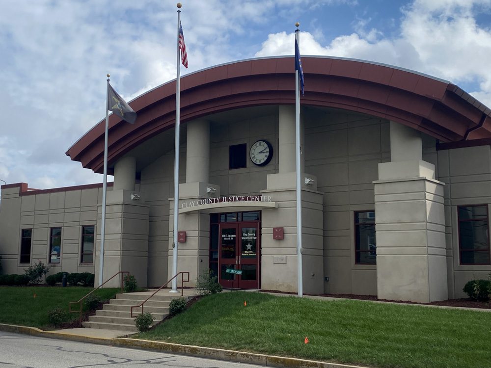 The front view of the Clay County Justice Center with a clock and three flags