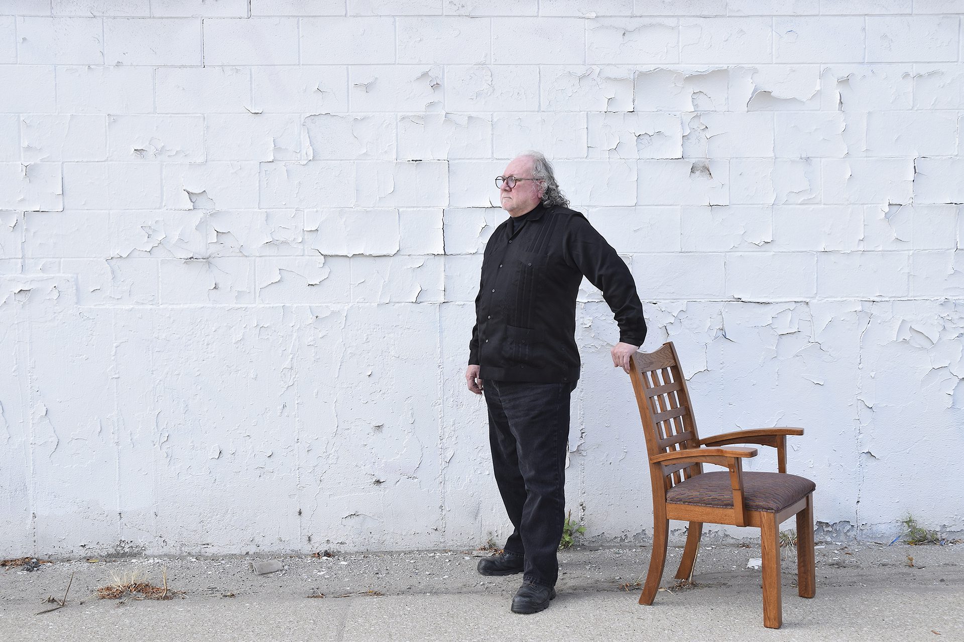 Gregorio Gomez with a white wall in the background and a wooden chair