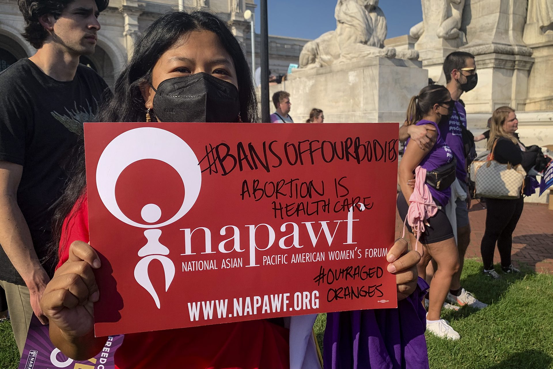 May Thach sostiene una pancarta roja en la que se lee &quot;#bansoffourbodies&quot; &quot;el aborto es atención sanitaria&quot; &quot;napawf&quot;