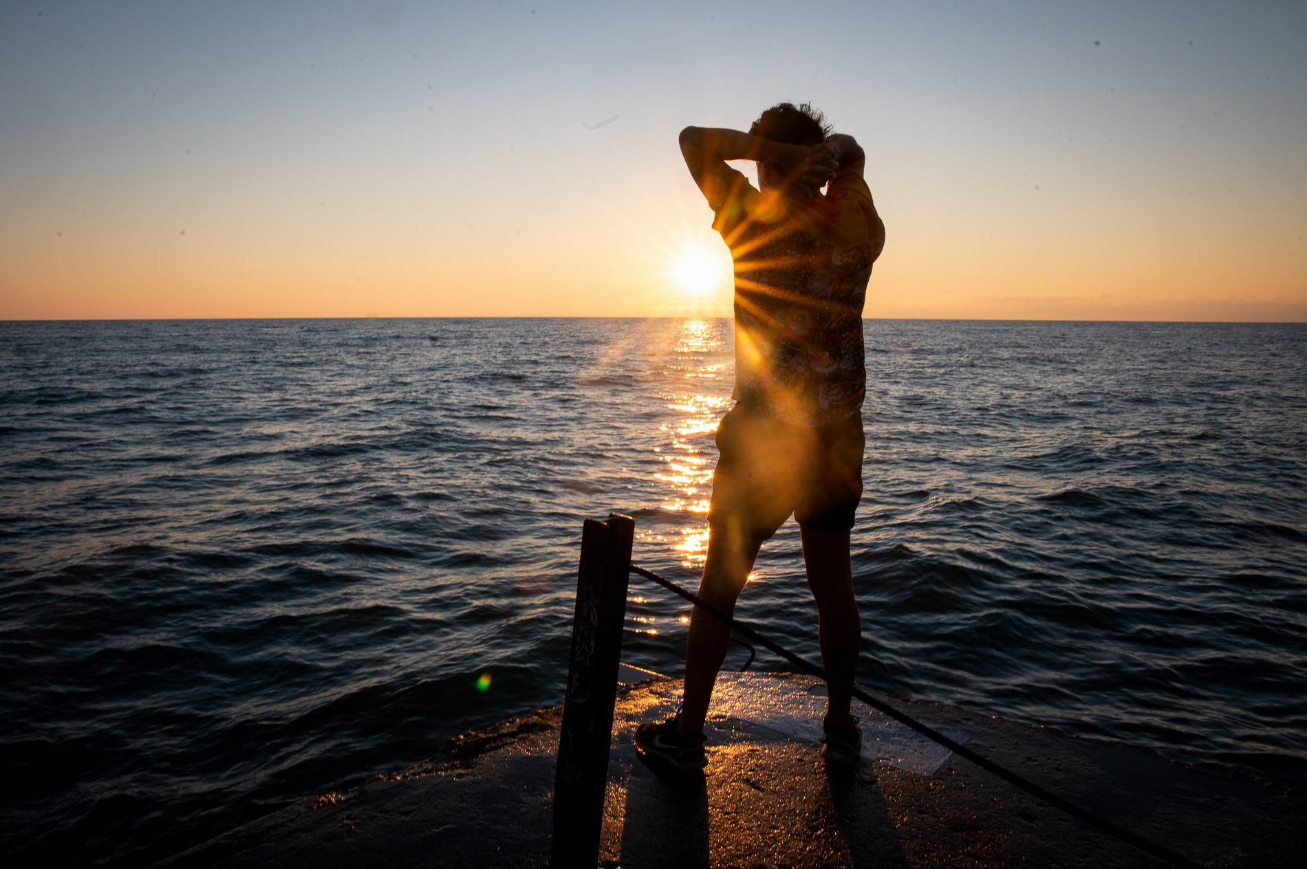 J Saxon dances on the Hollywood Beach Pier backlit by the sun and with the lake in the background