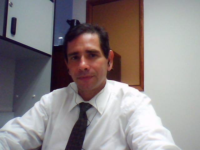 Frank Sandoval en su despacho con un traje blanco abotonado y una corbata