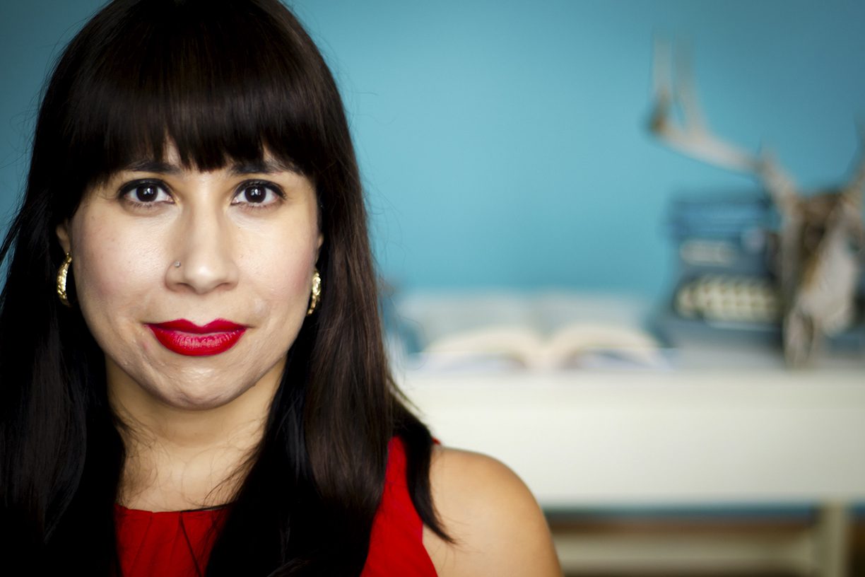 Erika Sanchez wearing red lipstick and a red top, blue background