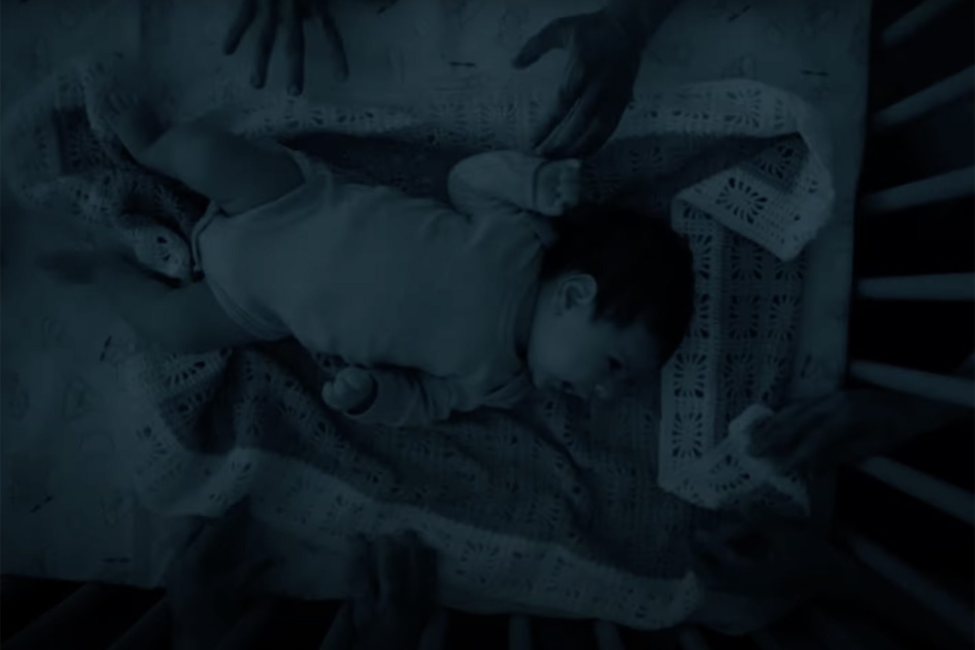 a baby in a crib with hands reaching for it
