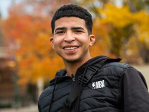 Maikel wearing a black NVA jacket and smiling with fall leaves