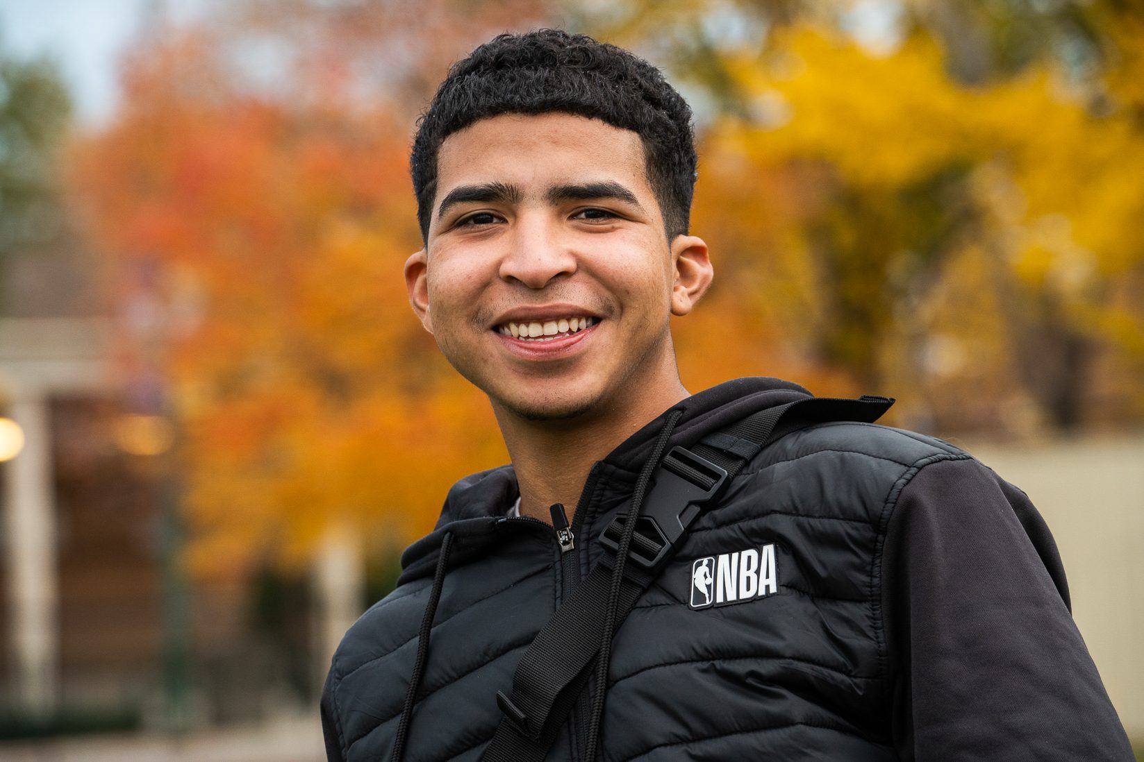 Maikel wearing a black NVA jacket and smiling with fall leaves