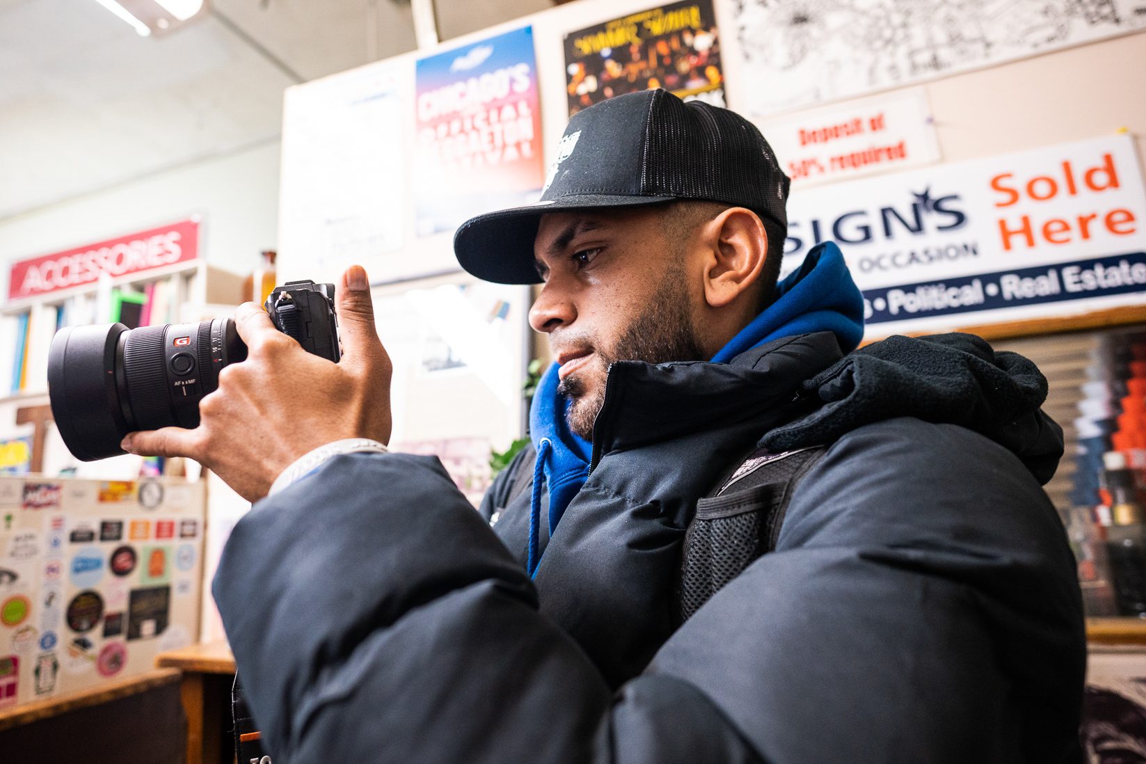 Jesus David Lucena Castillo looks at the back screen of a camera wearing a black puffy coat and cap