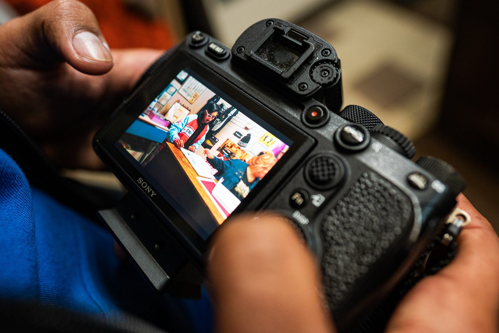 The back screen of a camera shows an image of the Kid interacting with someone else sitting at a table