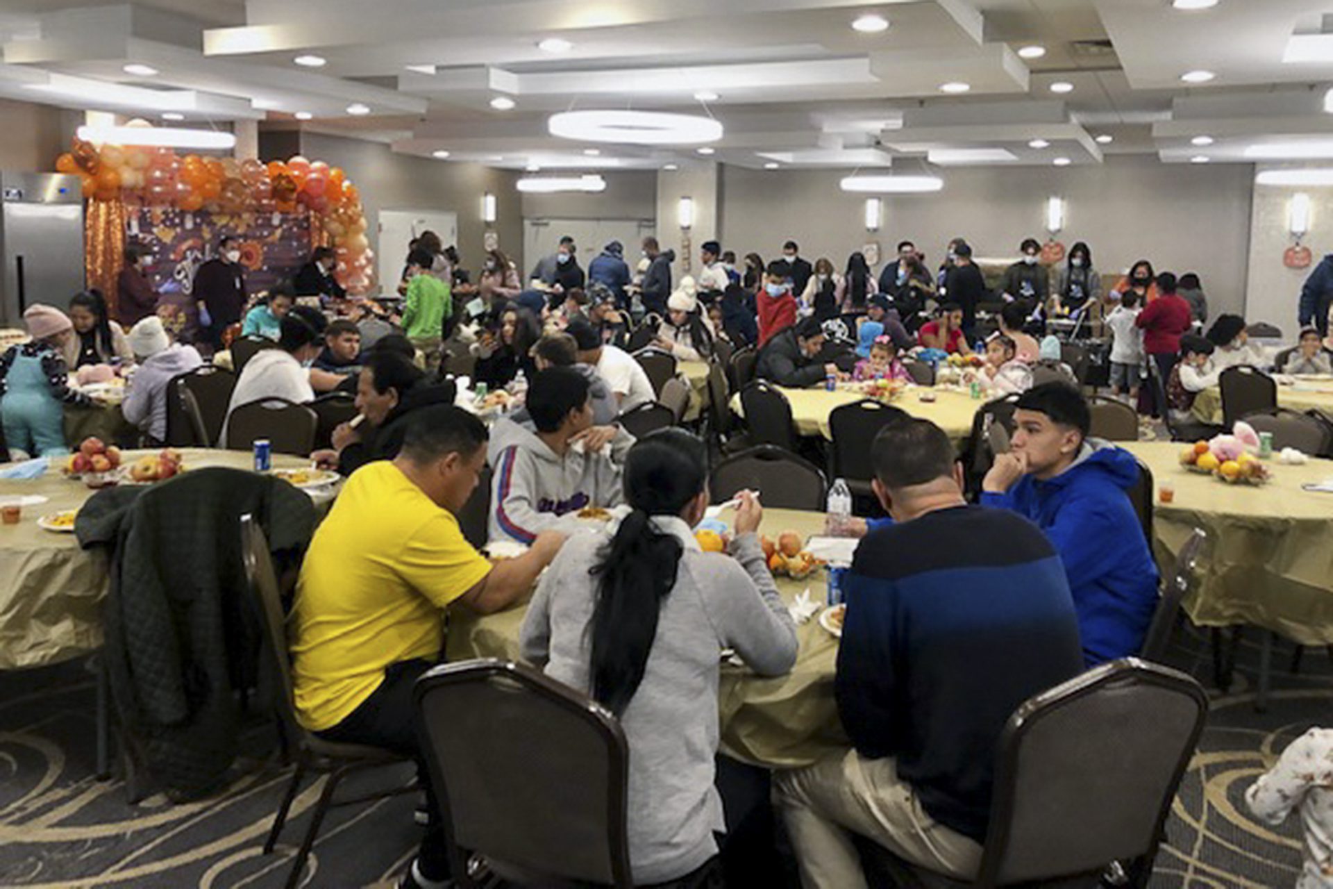 migrants at tables in a salon with thanksgiving decorations eating meals
