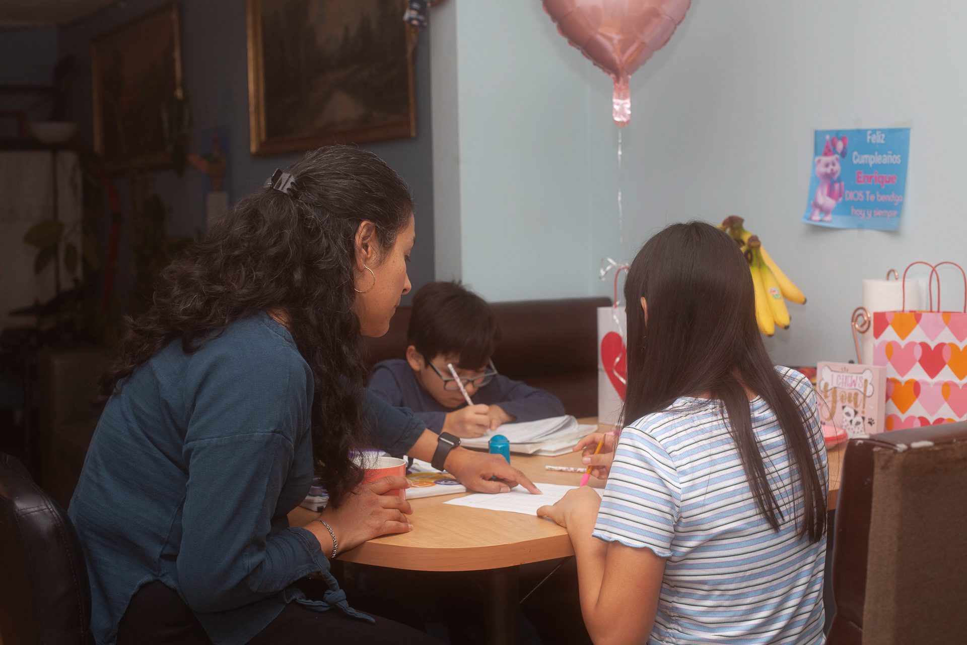 a mother and her two children sitting at the kitchen table reviewing homework