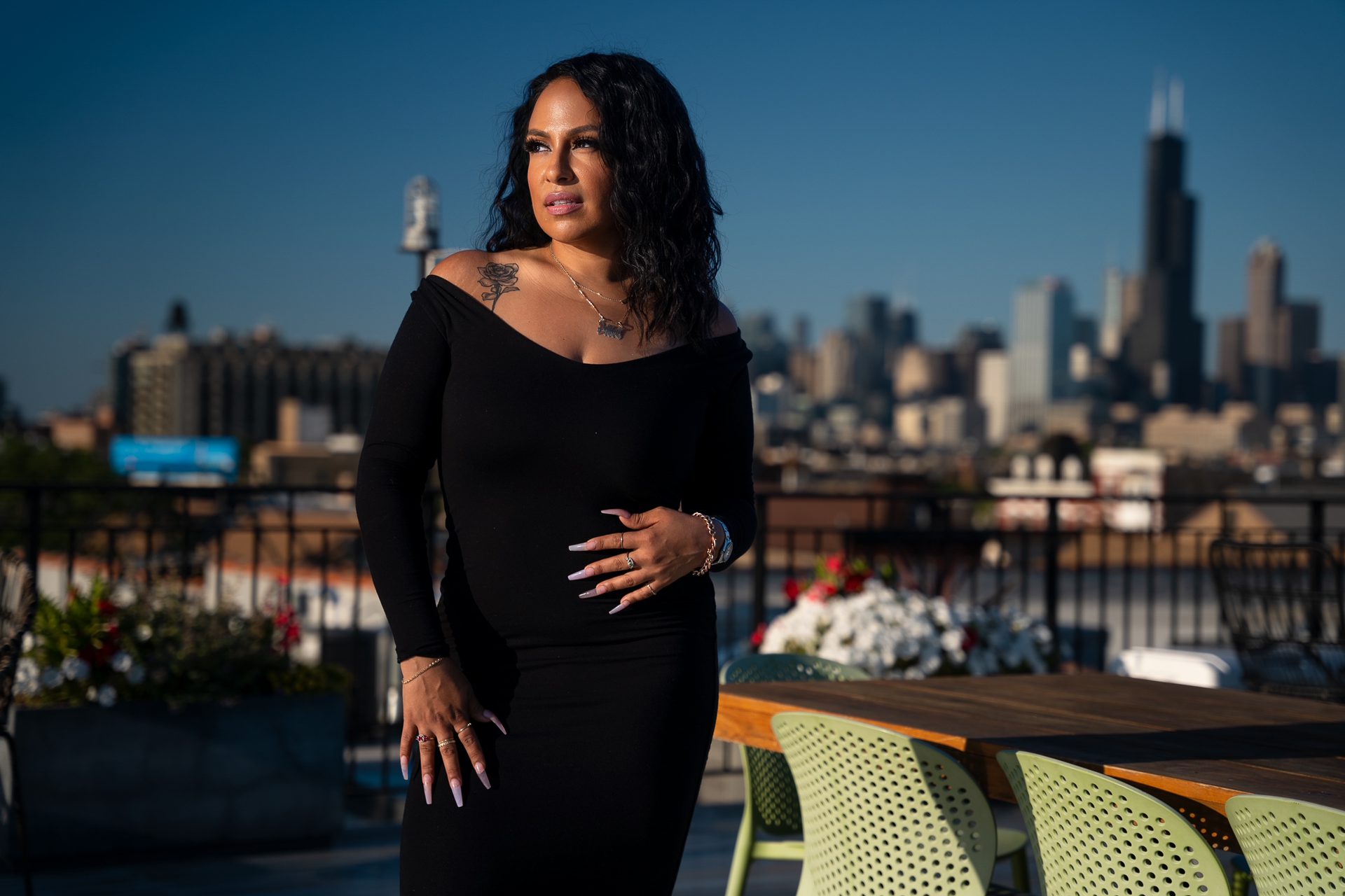 Delilah Martinez con un vestido negro, uñas moradas, un tatuaje de una rosa y el skyline de Chicago de fondo.