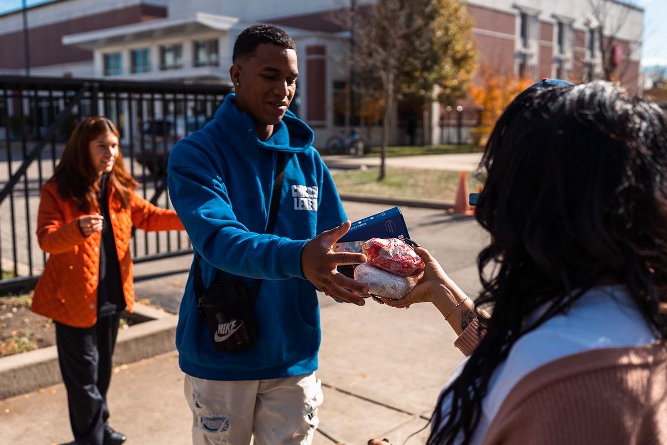 A man in a blue fleece accepts a breakfast sandwich while standing outside on the sidewalk